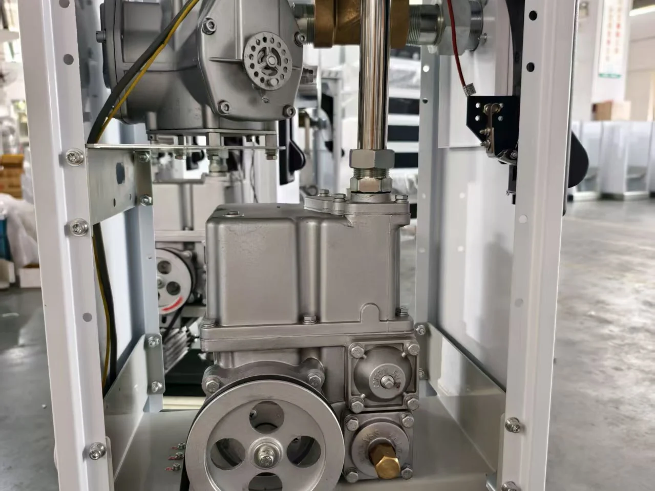 The hydraulic set inside a T-series dispenser during assembly: J6 flow meter and brass valve on the upper shelf, CP8 pump body in the middle, drive pulley below